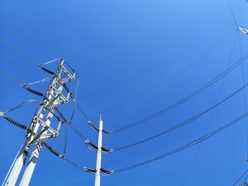 Low angle view of electricity pylon against clear blue sky