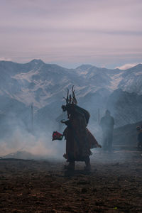 Young man in costume standing on field against cloudy sky during sunset