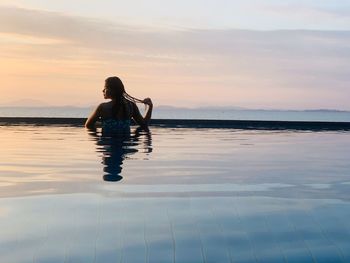 Rear view of woman in infinity pool against sky during sunset