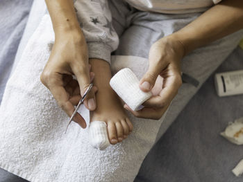 Mother bandages her child big toe. foot with bandaged finger. first aid in case of domestic injury.