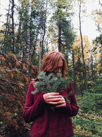 Young woman standing by tree in forest