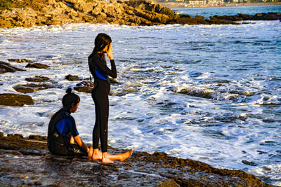 Side view of two young men on rock at beach