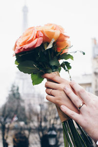 Cropped hand of people holding bouquet against sky