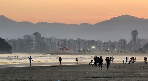 People at beach against sky during sunset