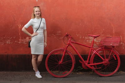 Portrait of beautiful woman standing by red bicycle against orange wall