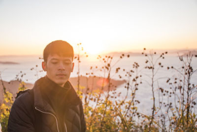 Portrait of young man standing against sky during sunset