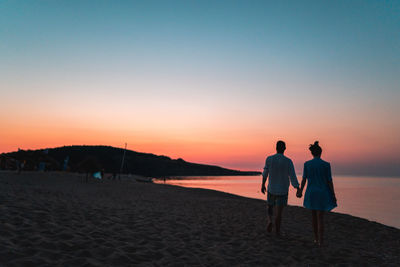 Rear view of men on beach against sky during sunset