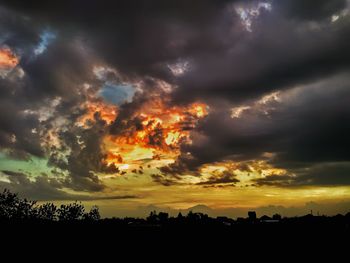 Low angle view of silhouette trees against dramatic sky