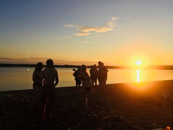 Silhouette people on beach against sky during sunset