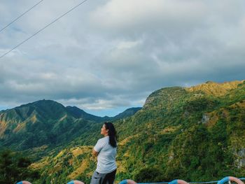 Woman standing against mountain and cloudy sky