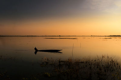 Silhouette man on boat in lake against sky during sunset