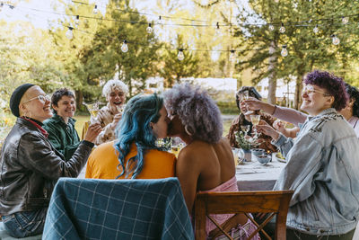 Affectionate transwoman kissing gay friend while sitting during dinner party in back yard