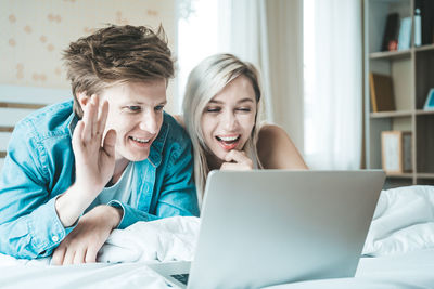 Portrait of smiling young man using mobile phone while sitting on bed
