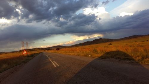 Empty country road against cloudy sky