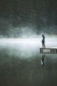Side view of man standing on pier over lake during foggy weather