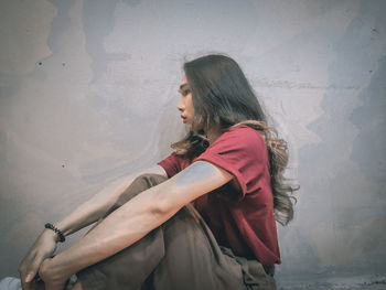 Side view of young woman standing against wall