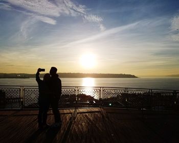 Silhouette couple standing at beach against sky during sunset