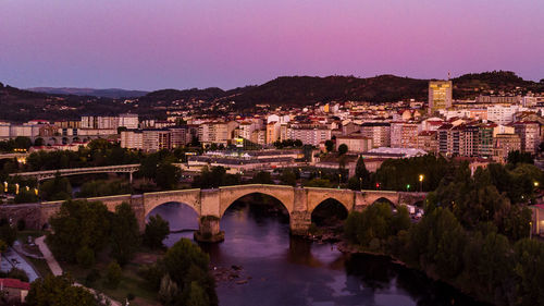 Arch bridge over river amidst buildings in city against sky at night