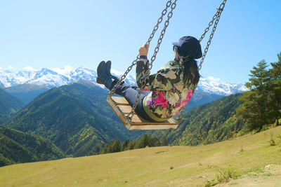 Rear view of woman sitting on swing against landscape