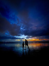 Silhouette woman standing at beach against sky during sunset