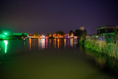 Illuminated buildings by river against clear sky at night