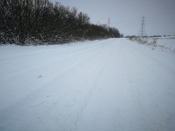 Snow covered road amidst field against sky