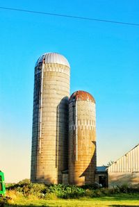 Low angle view of old silos against clear blue sky