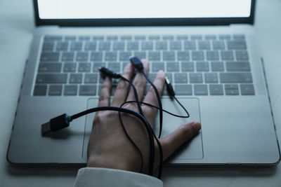 Cropped image of hand with cables on laptop