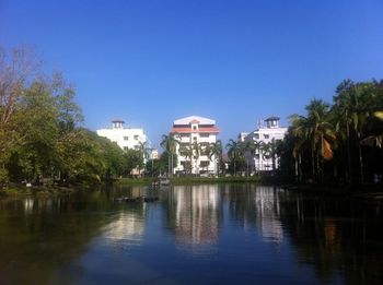 Reflection of trees and buildings in lake against blue sky