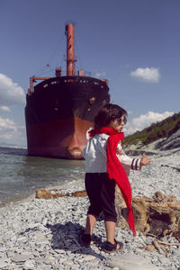 Fashionable boy child with long hair dance next to a large ship that ran aground near novorossiysk