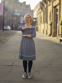 Full length portrait of woman gesturing while standing on footpath against buildings