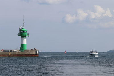 Lighthouse on sea by building against sky