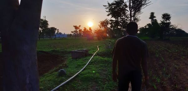 Rear view of man standing on field against sky during sunset