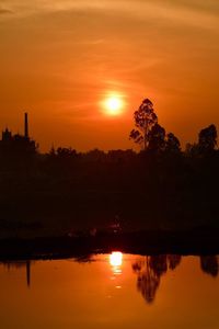 Silhouette trees by lake against romantic sky at sunset