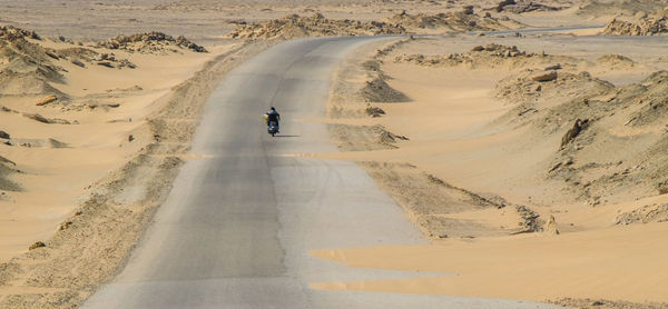 Rear view of man riding motorcycle on road at desert