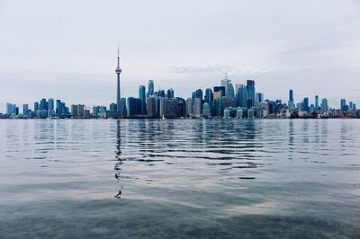 Cn tower with cityscape by river against sky