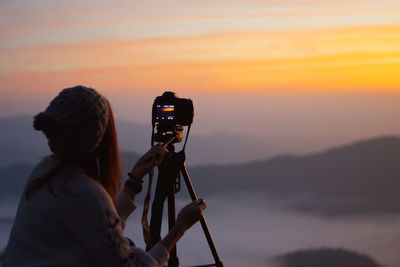 Low angle view of camera photographing against sky during sunset