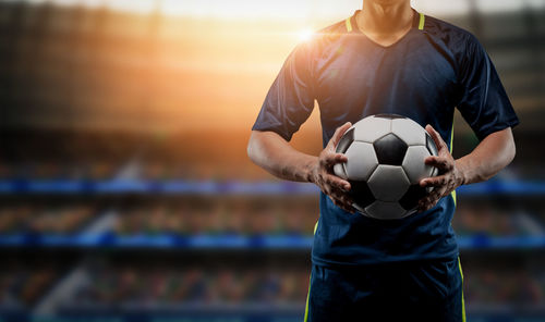 Man holding ball while standing on soccer field