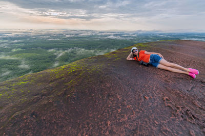 Full length of woman lying by cliff against landscape