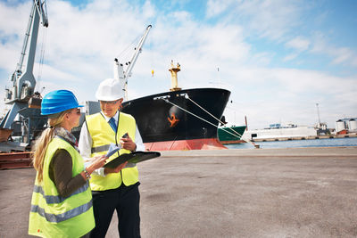 Colleagues wearing hardhat discussing at harbor