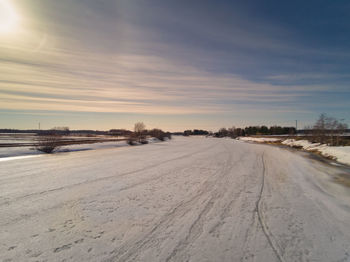 Snow covered road against sky during sunset
