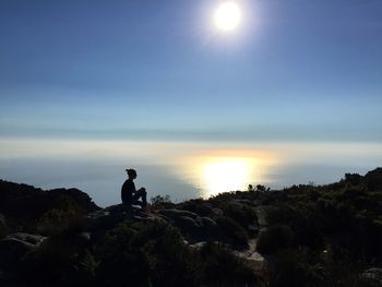 Silhouette man sitting on rock against sky during sunset