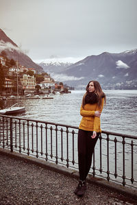 Woman standing on railing by snowcapped mountain against sky