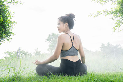 Young woman sitting on grass against sky