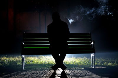 Rear view of man sitting on bench at night