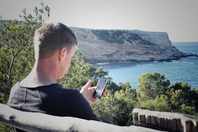 Man using mobile phone by sea against sky