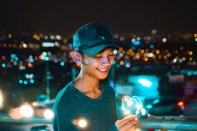 Portrait of smiling young woman against illuminated city at night