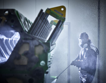 Worker cleaning engine block in washing bay