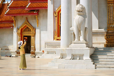 Female visitor taking pictures of guardian lion at wat benchamabophit in bangkok, thailand