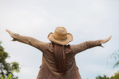 Low angle view of woman with arms outstretched standing against sky